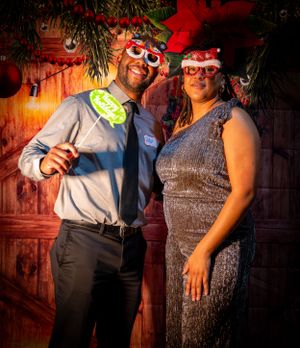 Couples posing together at a festive holiday party against a red-lit wooden backdrop.