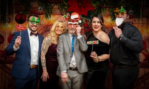 Group photo of party guests wearing festive attire and masks against a holiday backdrop.
