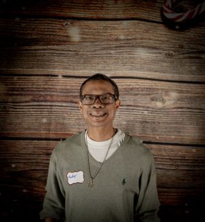 Individual wearing casual grey sweater photographed against wooden paneled wall.