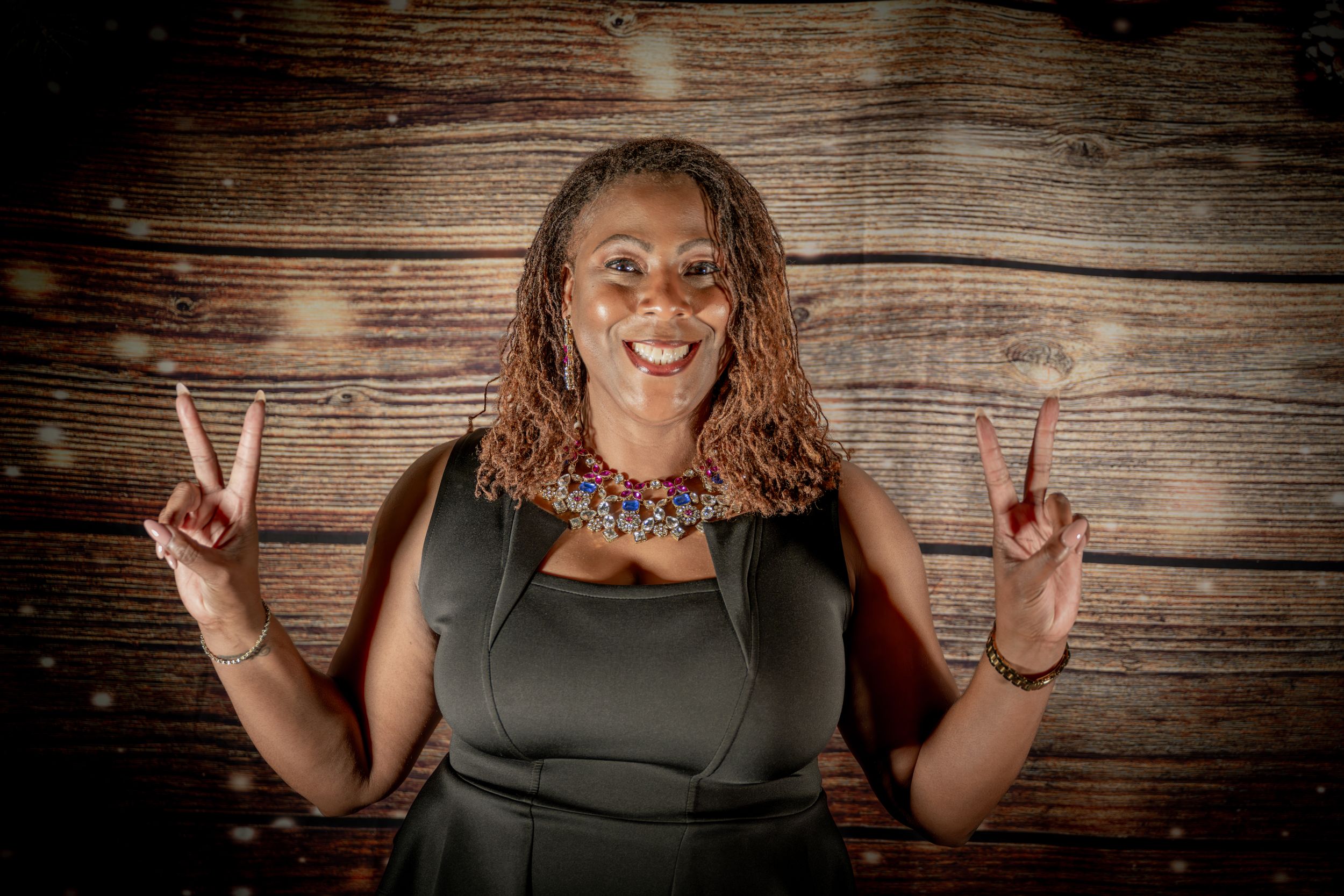 Joyful person making peace signs against rustic wooden background with holiday decorations.