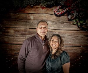 Couple posing together against wooden backdrop with holiday decorations.