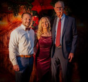 Group in formal attire poses together at festive holiday party with red ambient lighting.