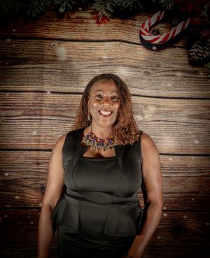 Formal portrait against wooden backdrop showing person in elegant black dress with statement necklace.