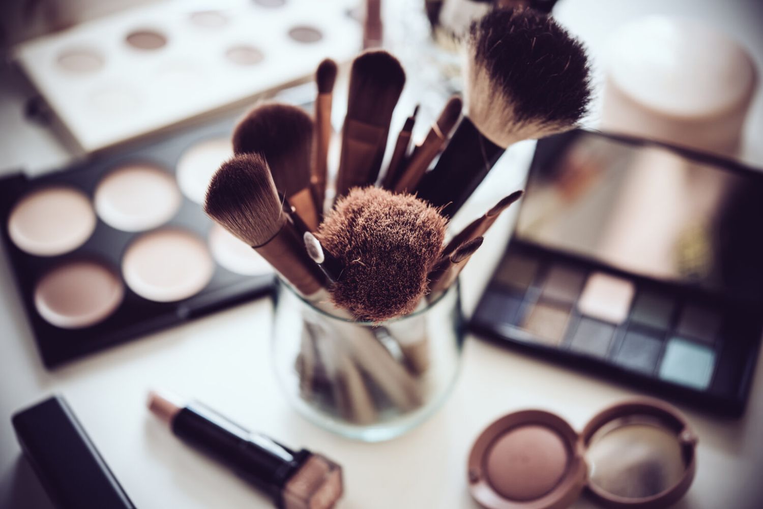 Collection of makeup brushes and cosmetics arranged on white surface.