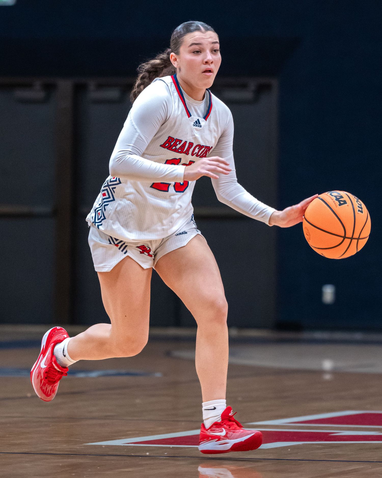 Basketball player in white jersey dribbles down court during intense game action.