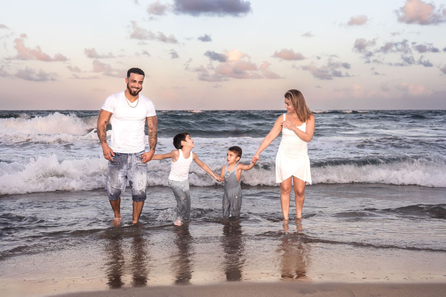 Family holding hands and walking together along beach at sunset.