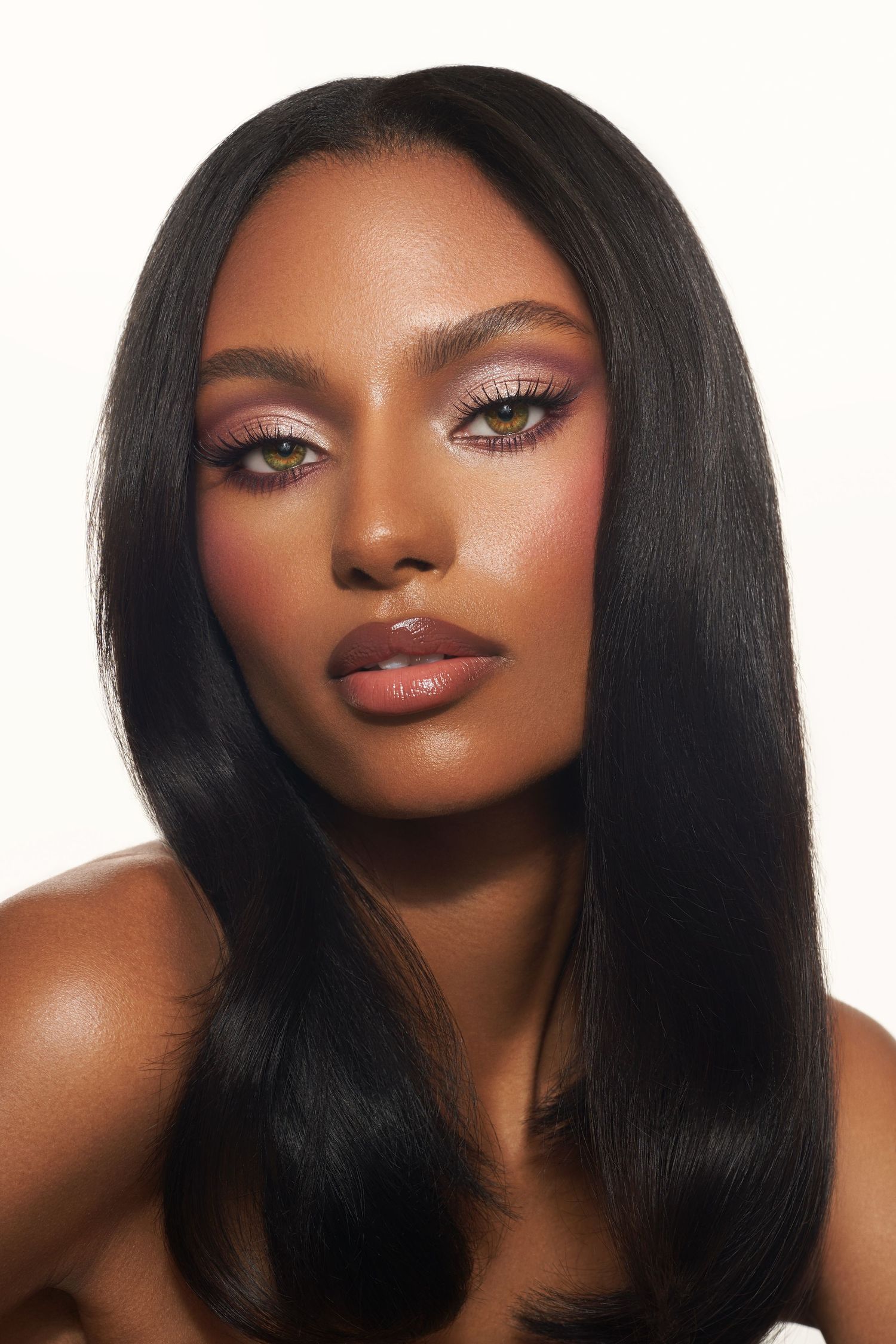 Glamorous beauty portrait with long straight hair and warm-toned makeup against white background.