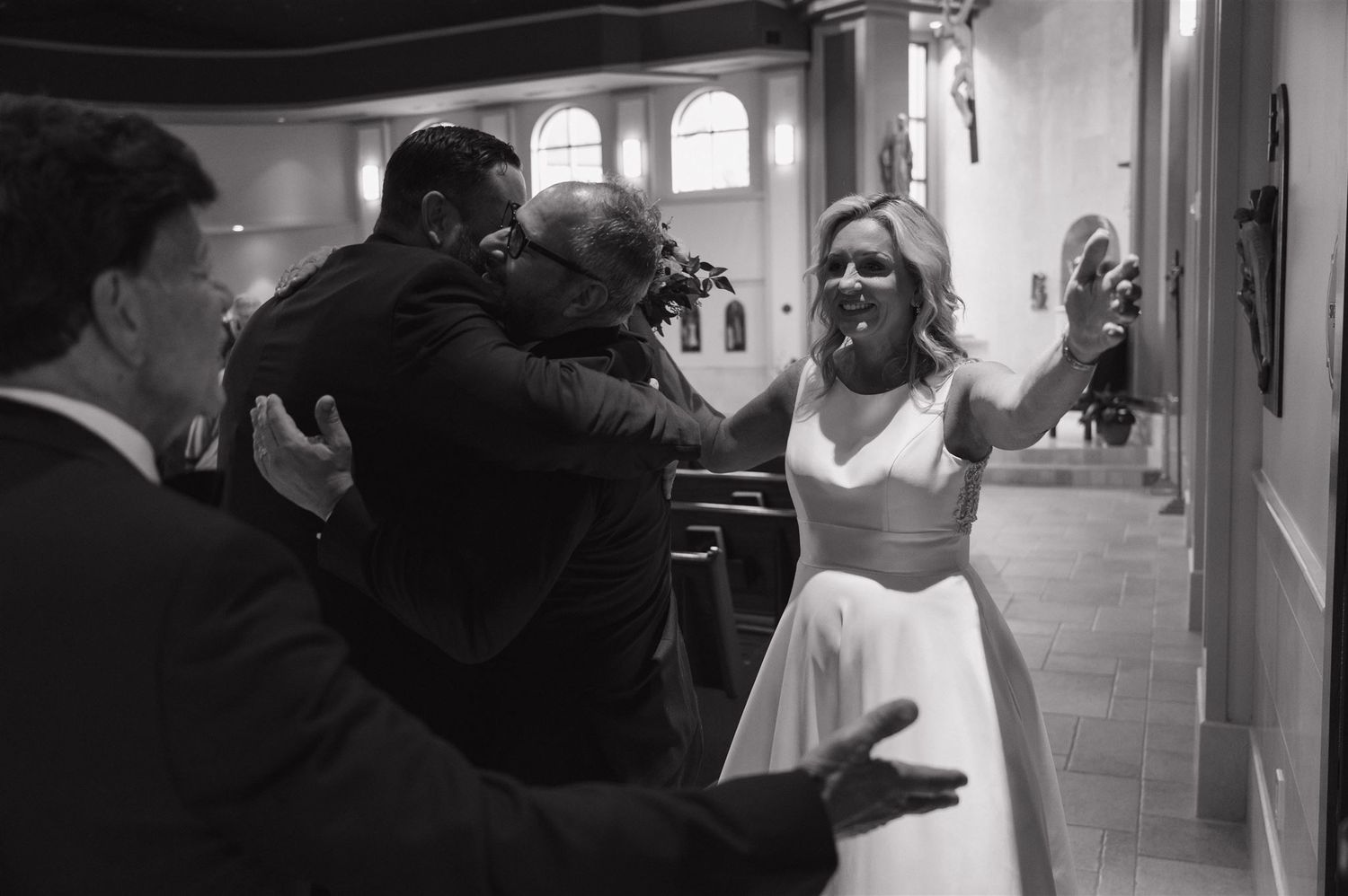 Black and white photo capturing joyful celebration in an elegant hallway with arched windows.