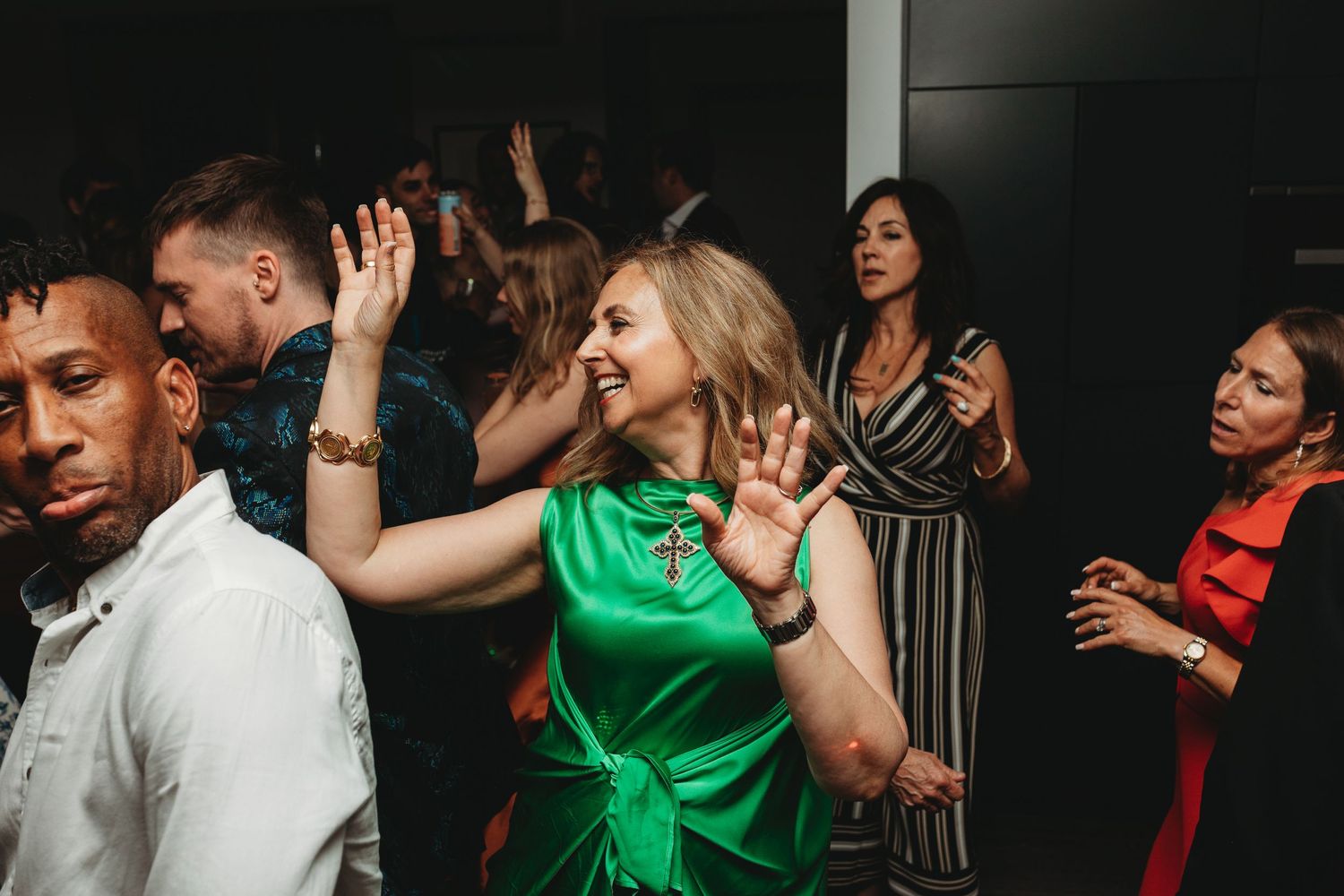 Party guests dancing and celebrating enthusiastically in a dark venue with one wearing a vibrant green dress.