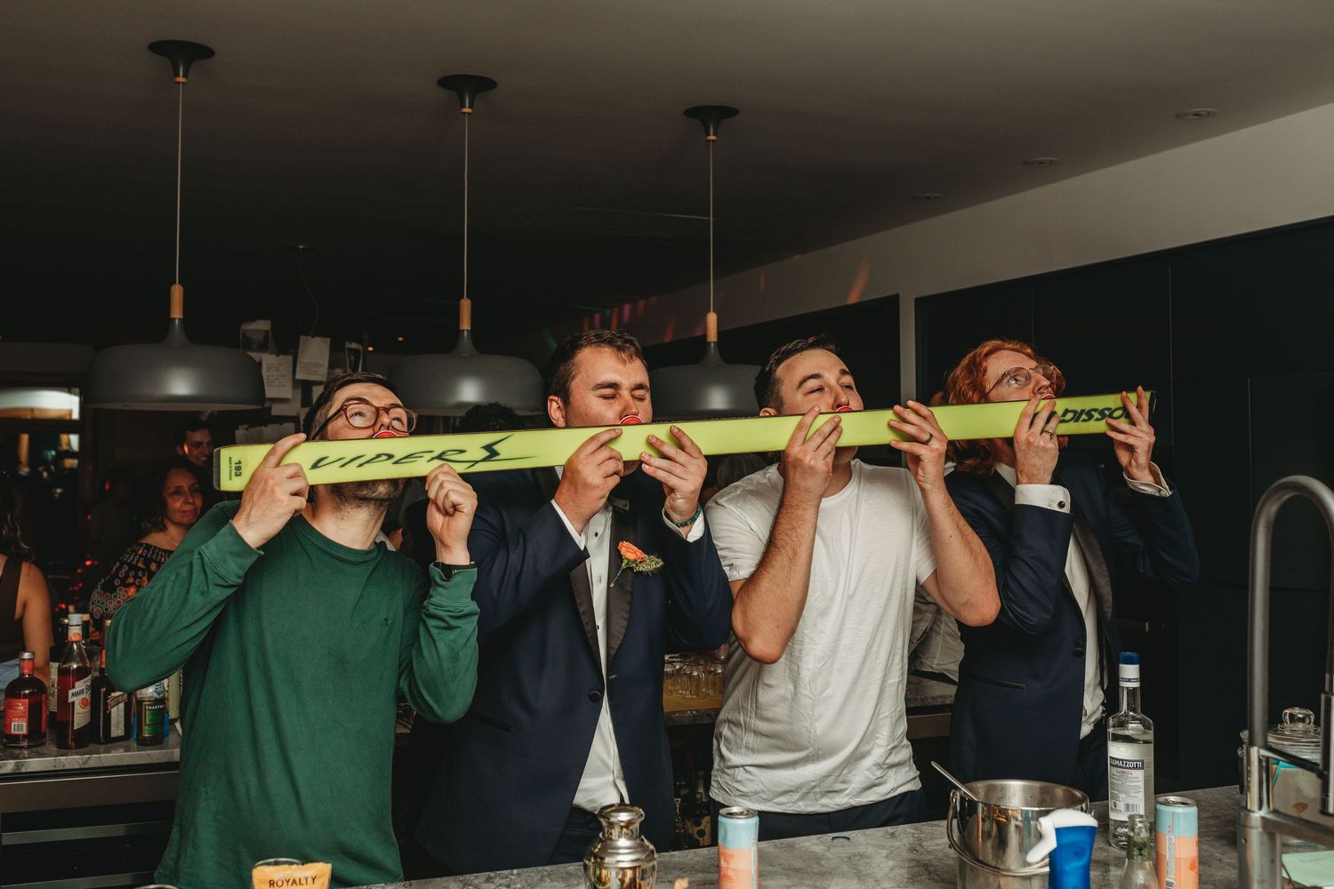 Group of people at a party sharing a drink from a long green glass bottle.