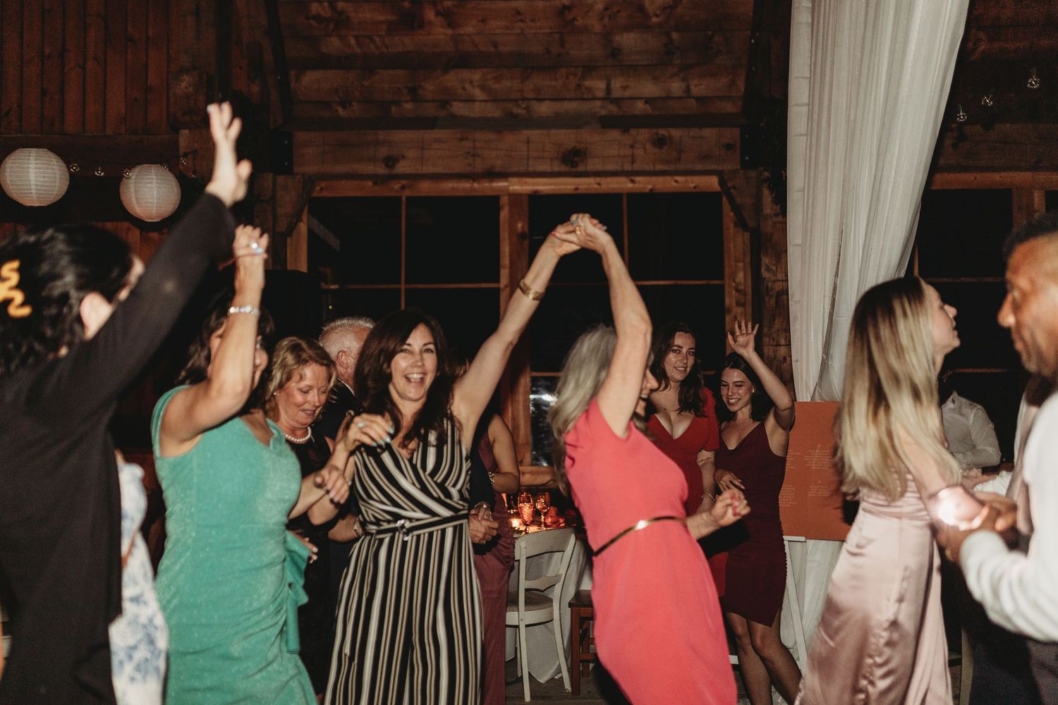 Wedding guests dancing and having fun at a rustic wood-paneled reception venue.