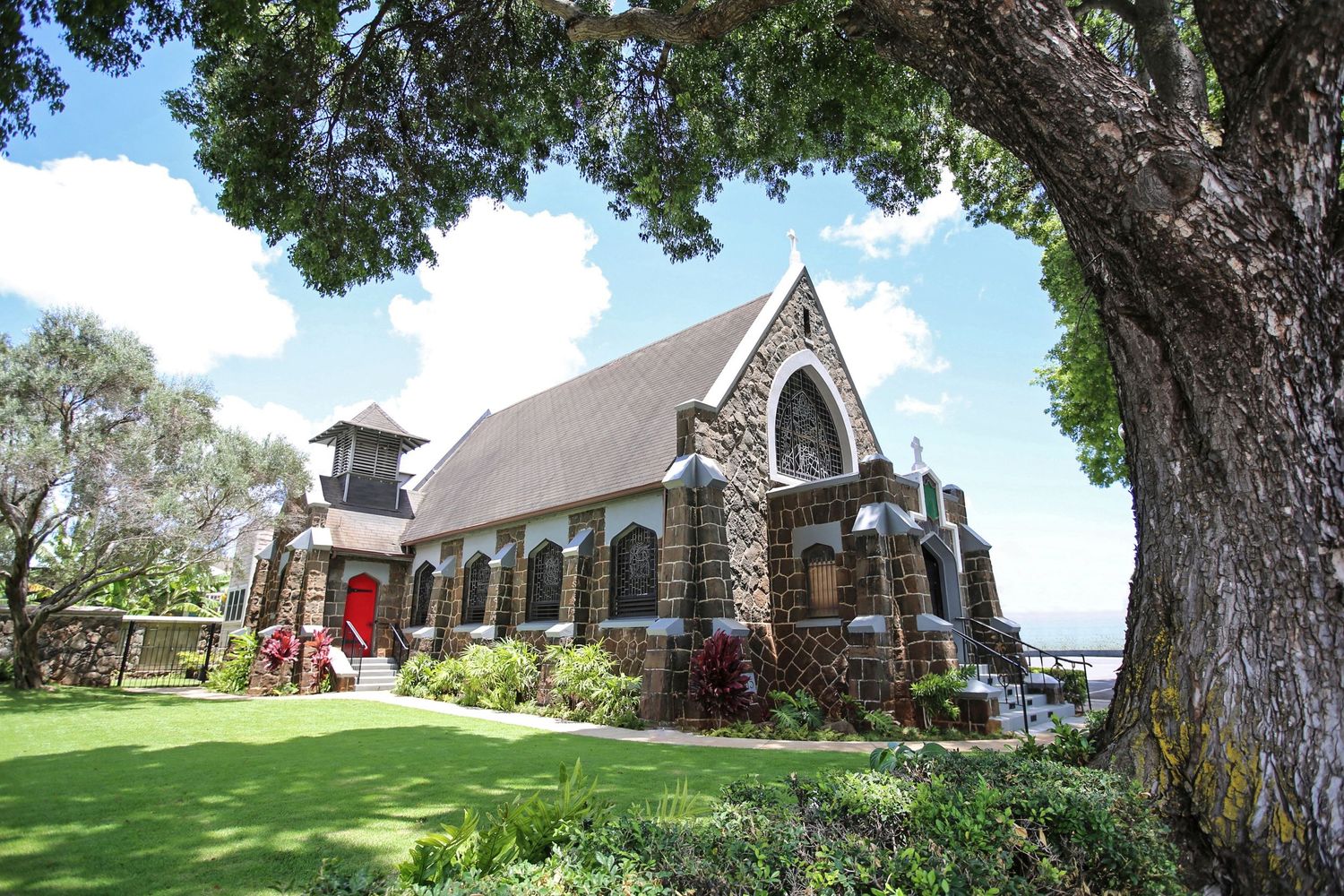 Stone church with red door surrounded by lush tropical gardens and large trees under a bright blue sky.
ハワイウェディング
ハワイ挙式
