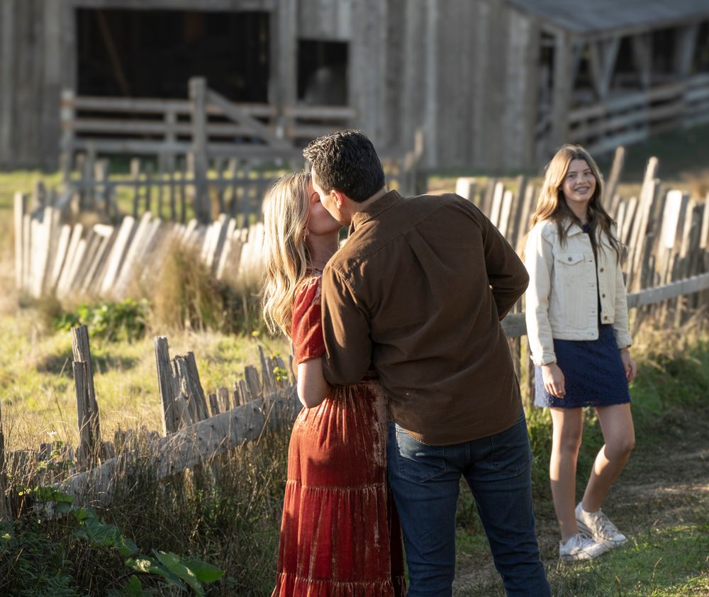 A couple embraces near an old barn with rustic fence posts during golden hour. At The Sea Ranch Lodge in Northern California.