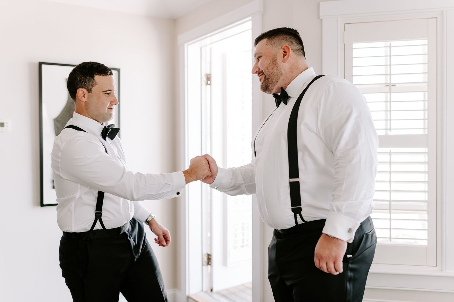 Two groomsmen in formal attire share a handshake while getting ready for a wedding.