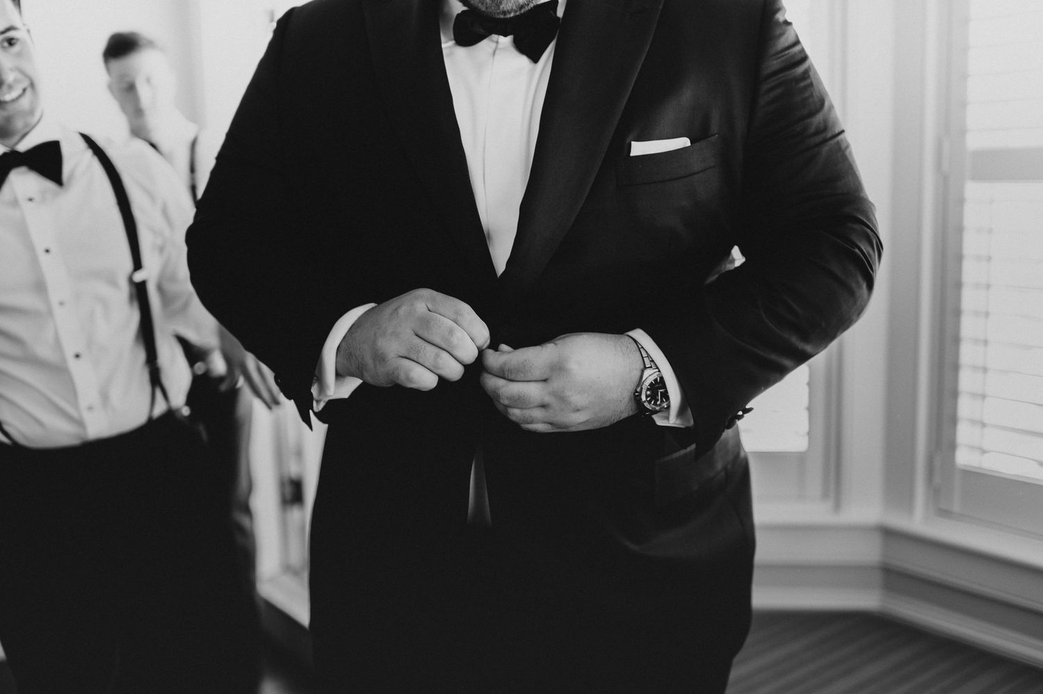 A close-up shot of a groom adjusting his tuxedo jacket and cufflinks.