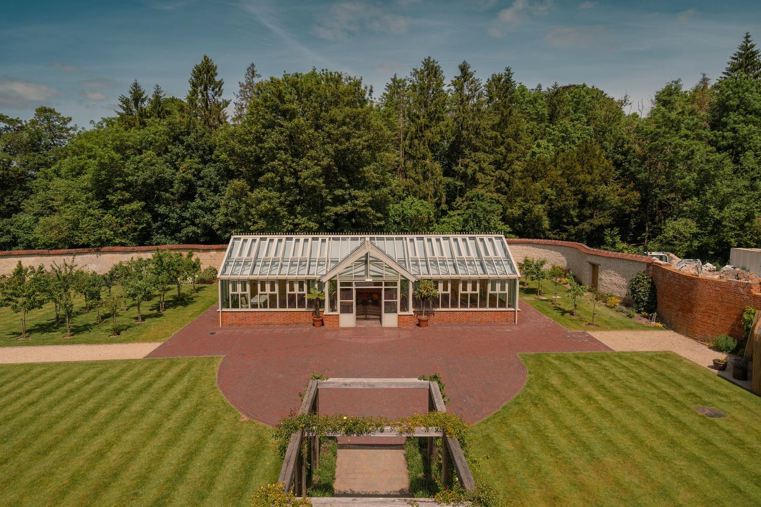 Elegant Victorian-style greenhouse with manicured lawn and brick pathways in a garden setting.