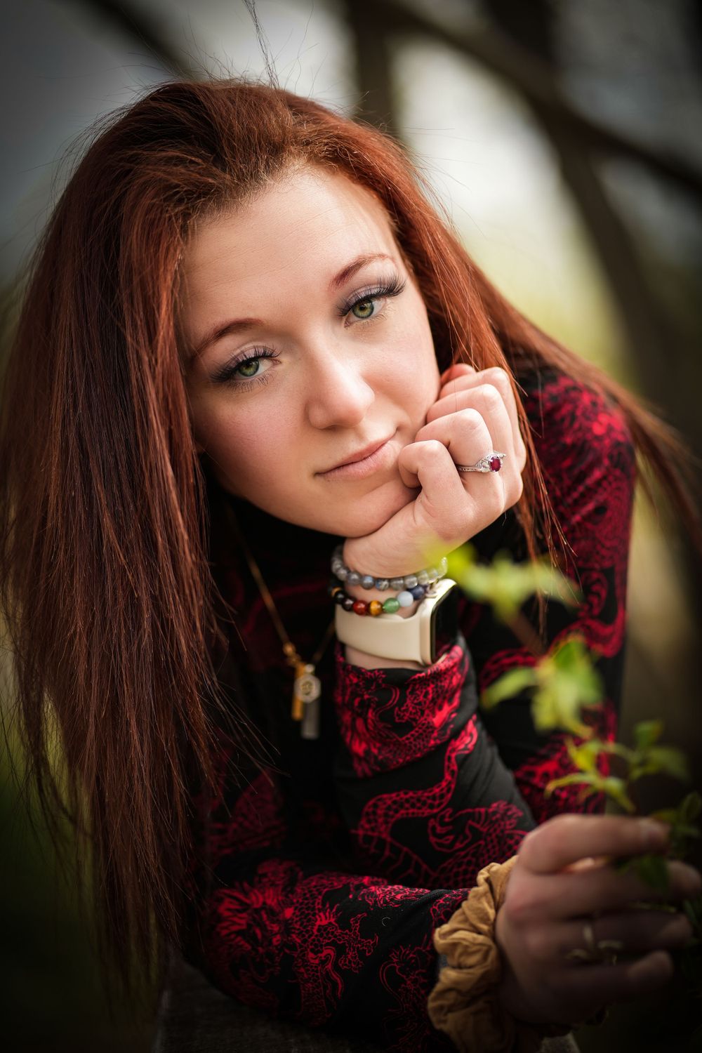 A thoughtful pose captured in soft lighting with burgundy clothing and natural backdrop.