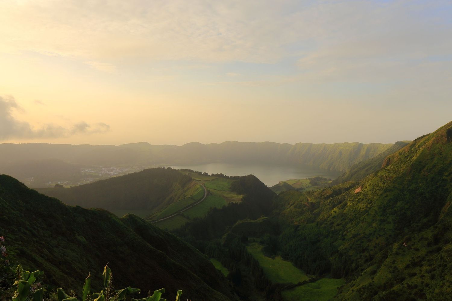Scenic mountain landscape at sunset with rolling green hills and distant valleys in soft golden light.