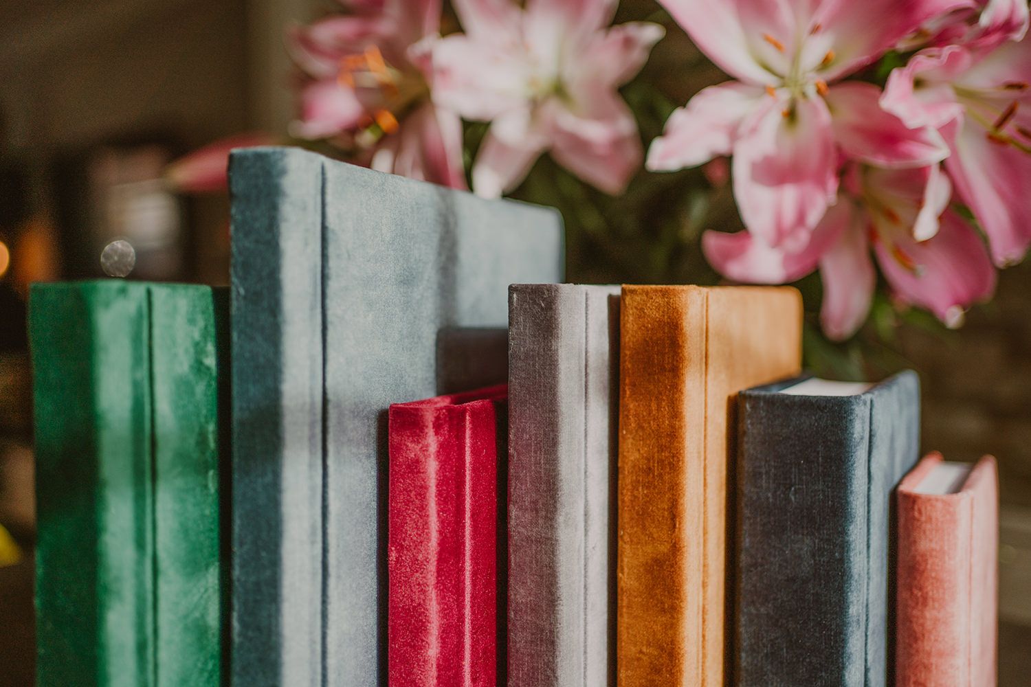 Collection of colorful vintage books lined up with pink flowers in the background.