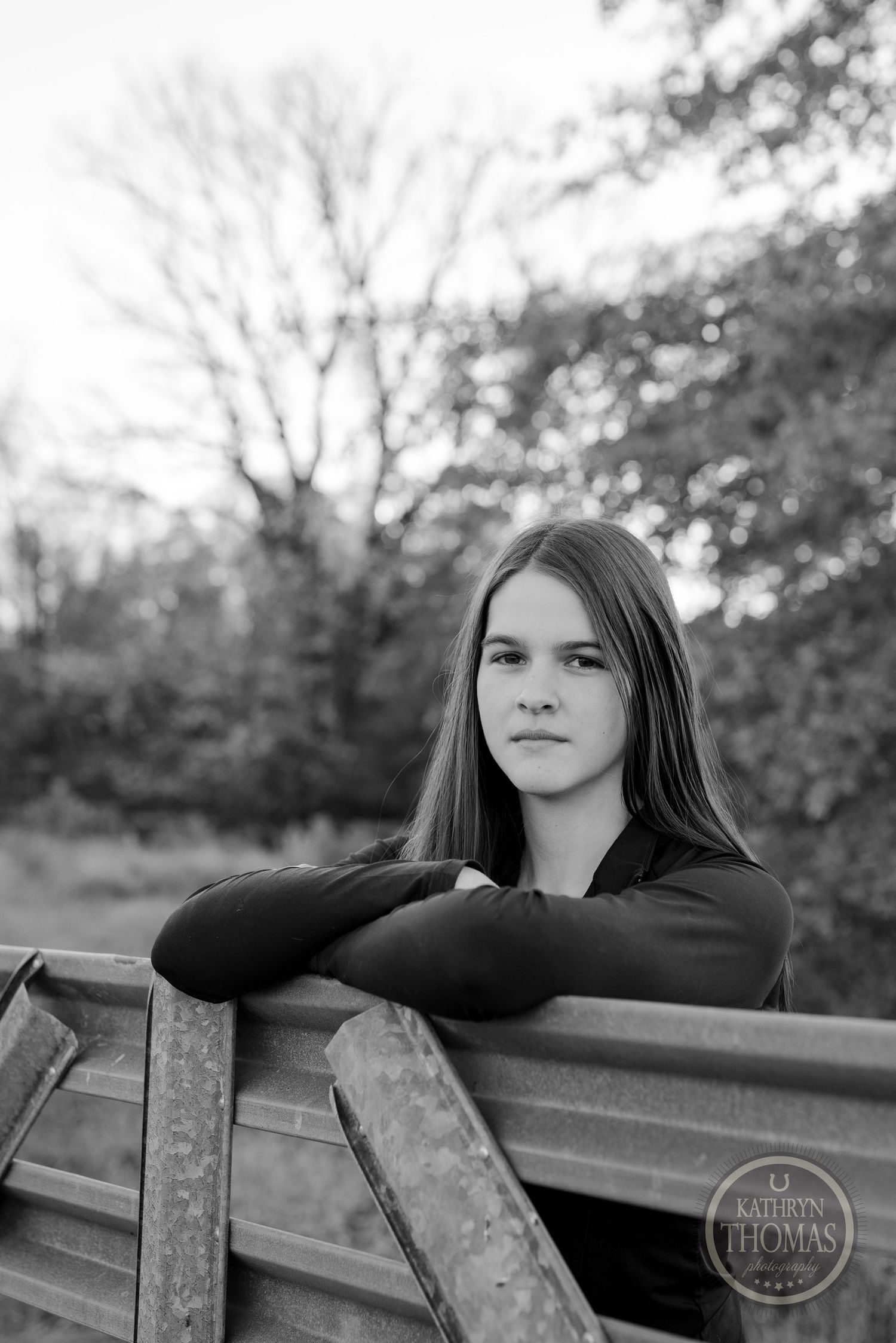 Black and white portrait leaning on wooden fence with soft natural lighting.