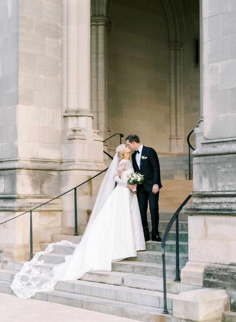 A wedding couple shares an intimate moment on stone church steps during their ceremony.