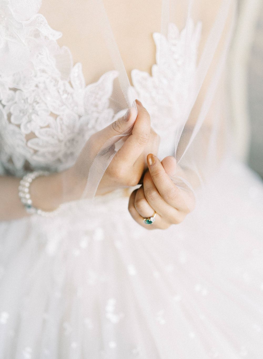 Close-up of bridal hands with pearl bracelet adjusting white lace veil.