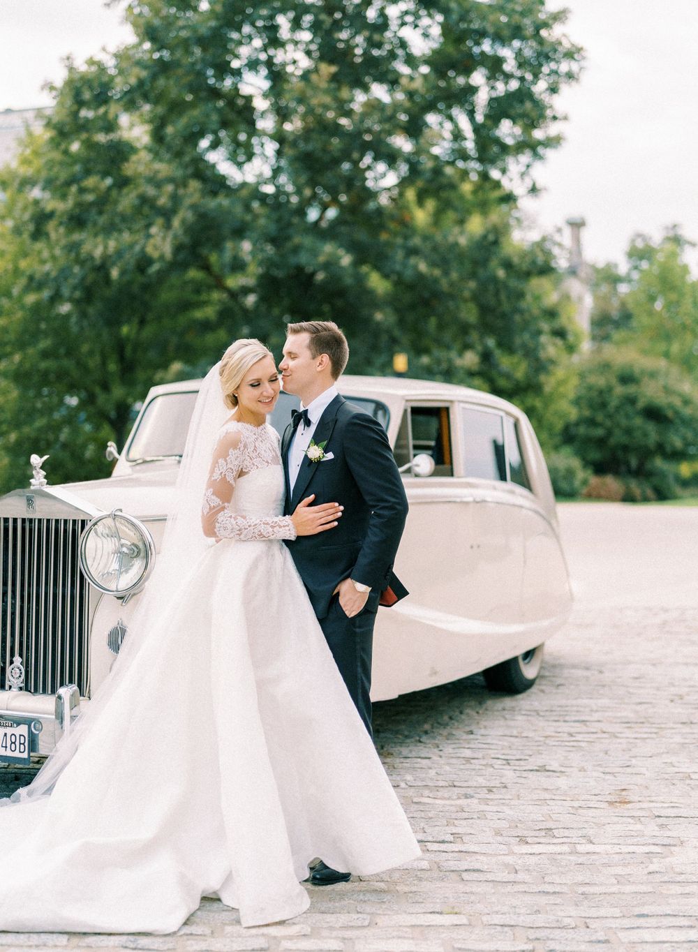 A classic wedding portrait with a vintage Rolls Royce in an elegant outdoor setting.