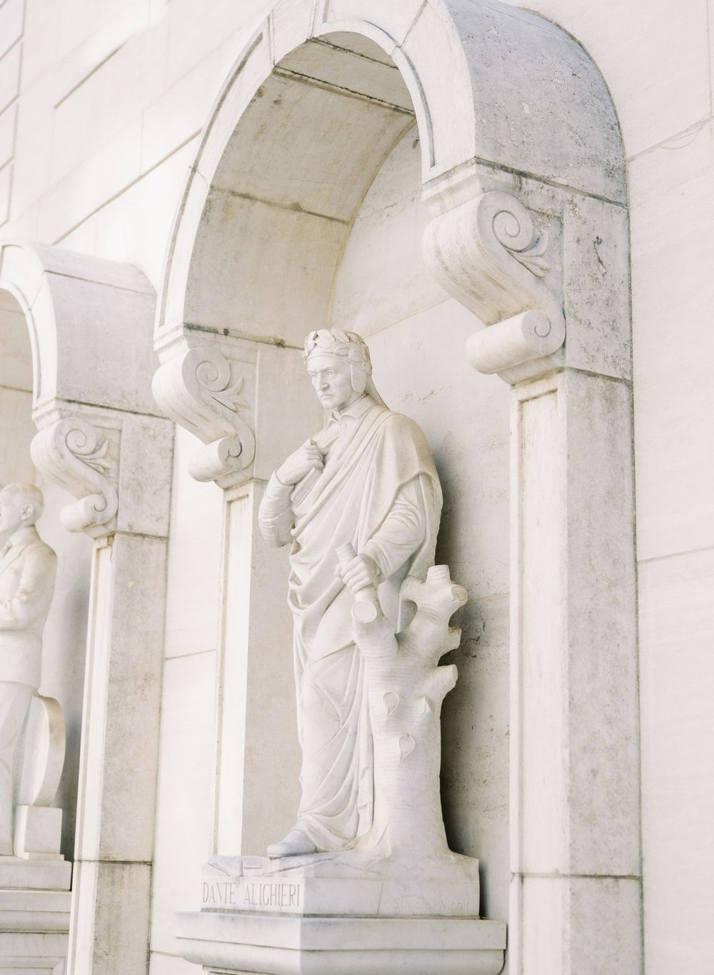 Classical white stone statue in an arched alcove of a building.