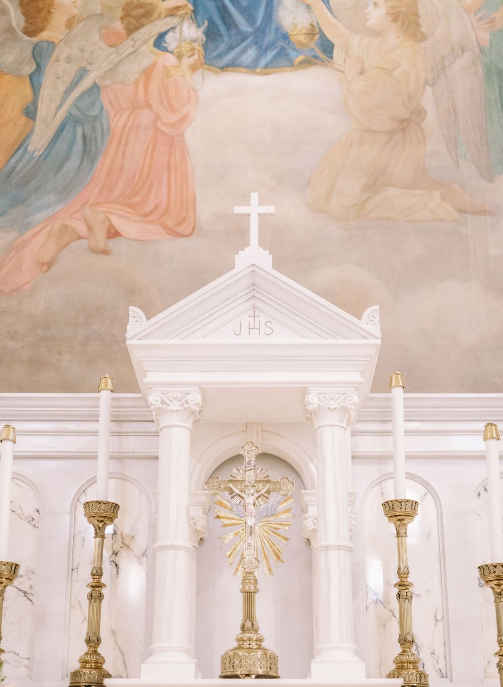 Ornate white church altar with crucifix, columns and religious mural painting above.