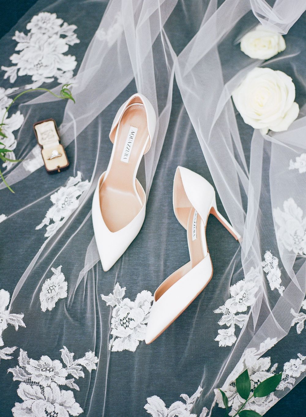 White bridal heels displayed on lace veil with delicate floral details.