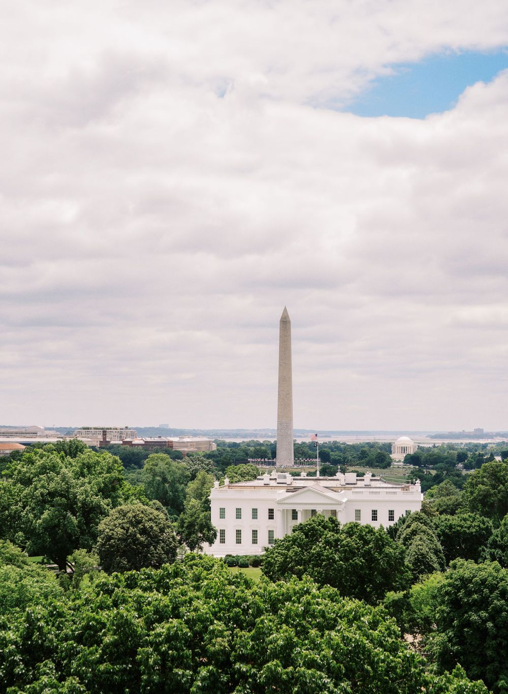 Aerial view of the White House and Washington Monument surrounded by lush green trees in Washington DC.