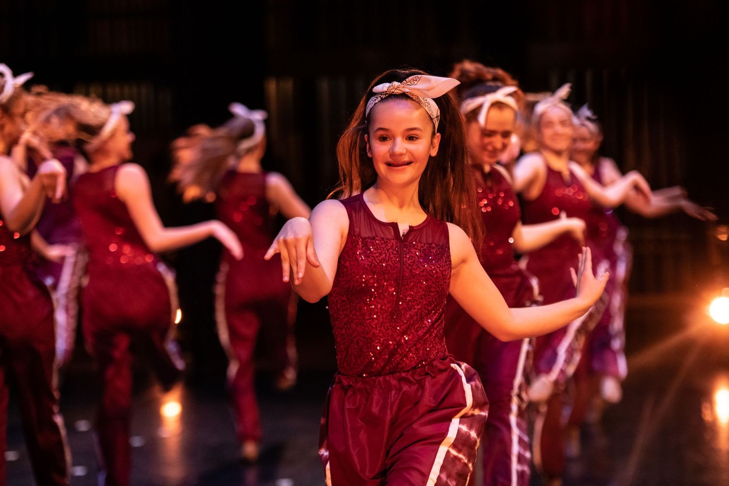 Dancers in sparkly red costumes perform on stage during a recital.