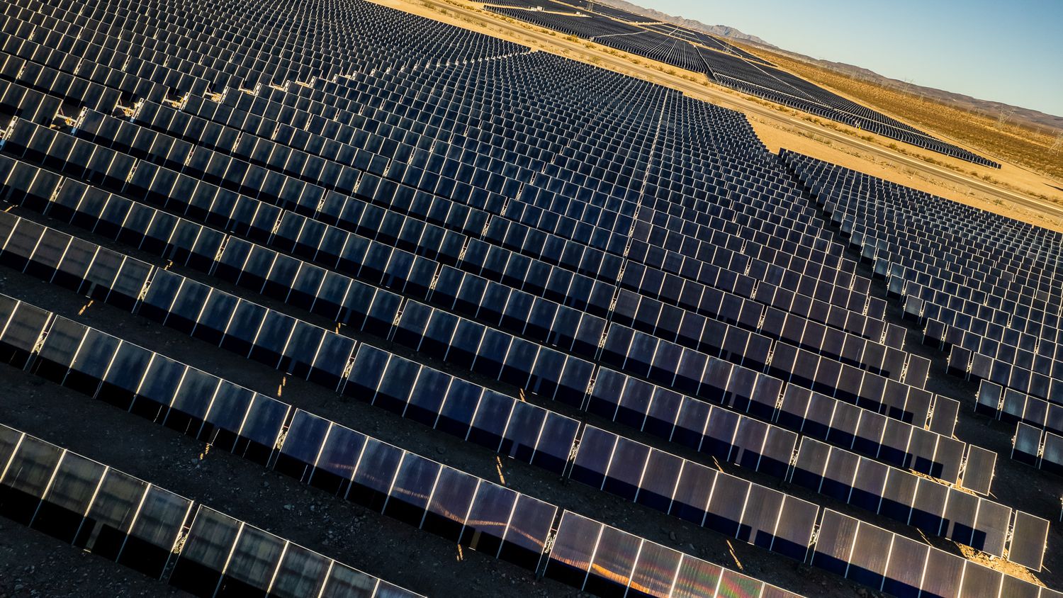 Large solar panel array installation stretching across desert terrain under blue sky.