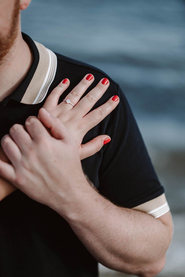 A hand with bright red nail polish rests on a shoulder wearing a black and white collared shirt.