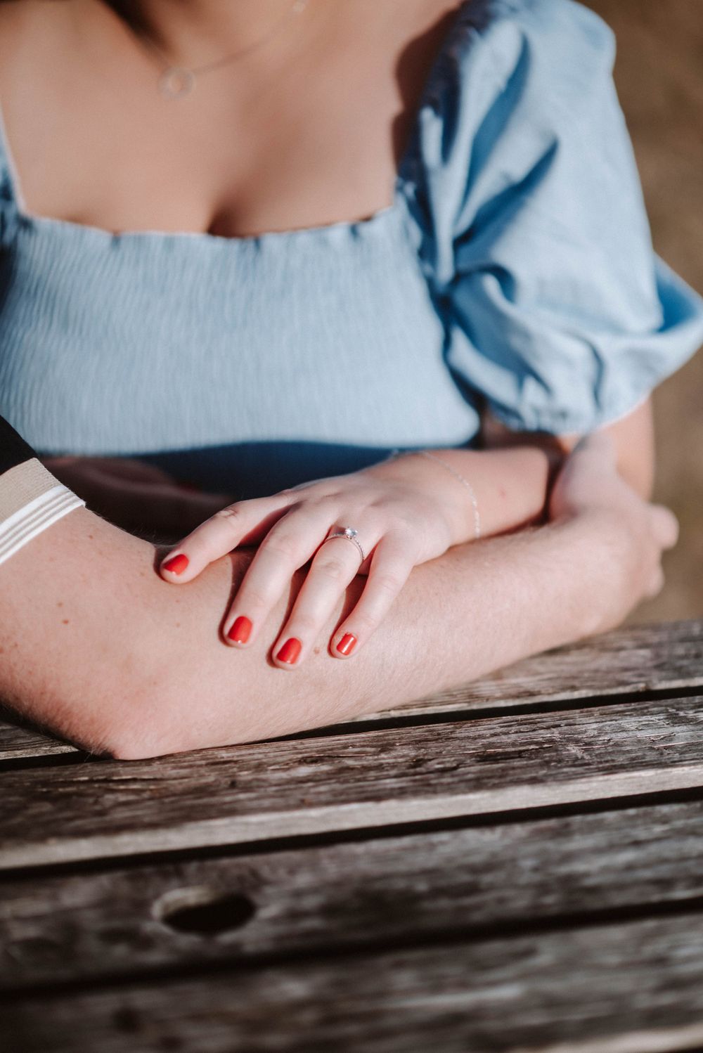 Close up of red painted fingernails and a light blue puff sleeve dress against weathered wood.