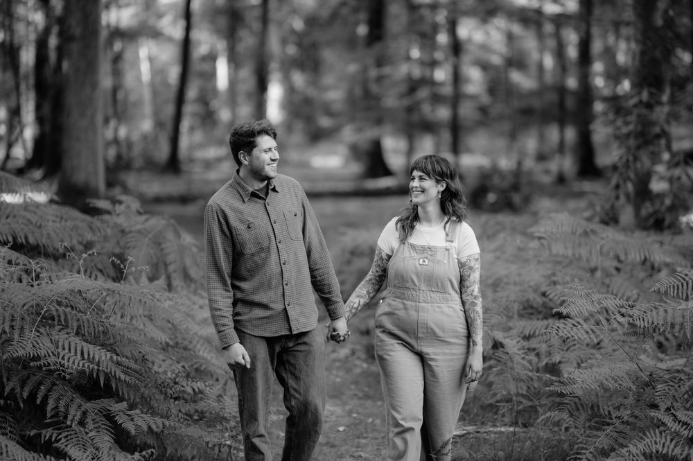 A couple walks hand in hand through a peaceful forest path in black and white.