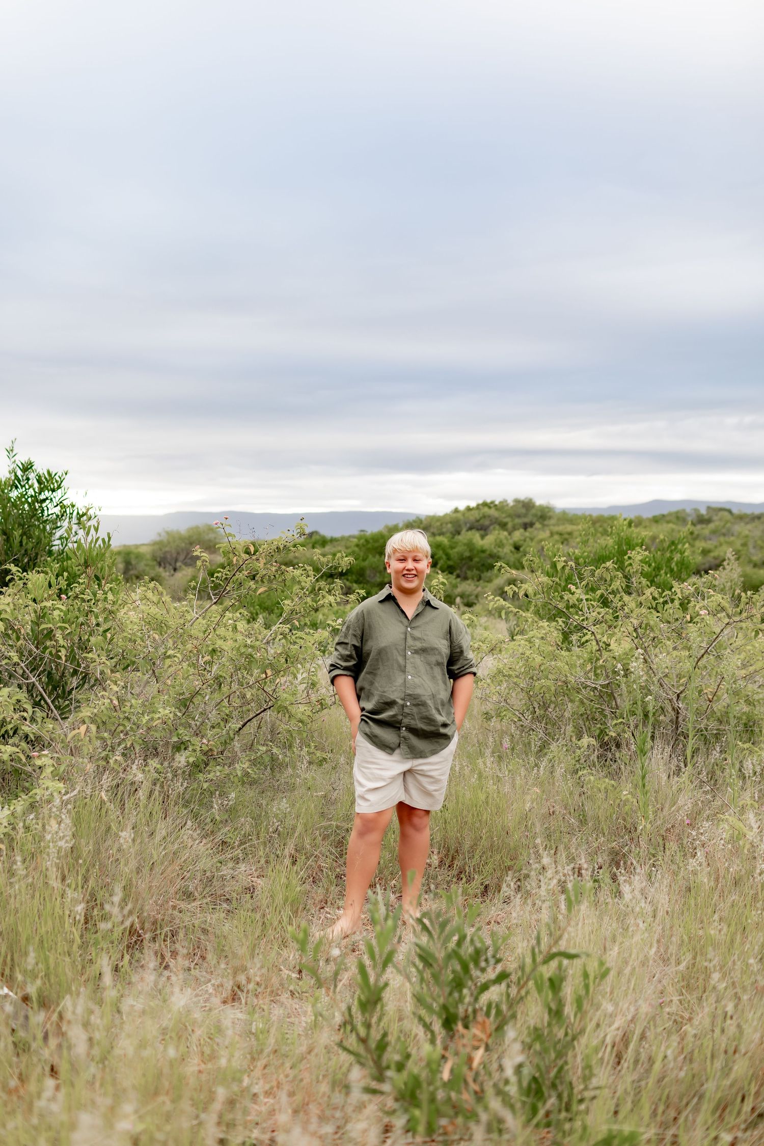 A casual outdoor portrait taken in a grassy field with rolling hills and cloudy skies in the background.
