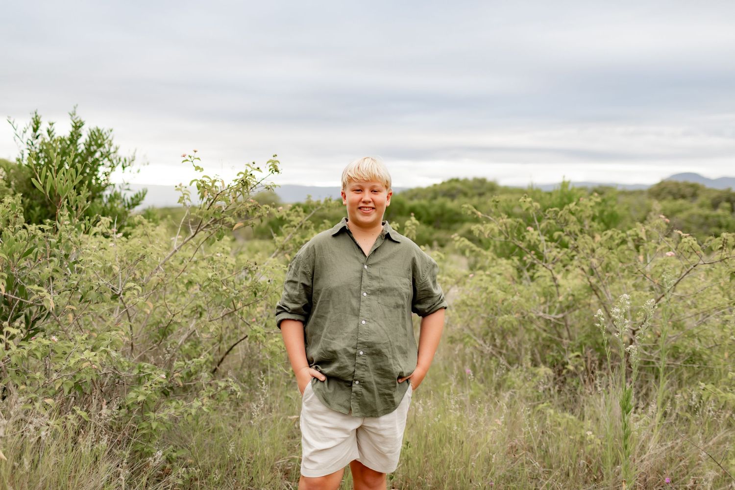 A relaxed outdoor portrait against a scenic backdrop of green brush and overcast sky.