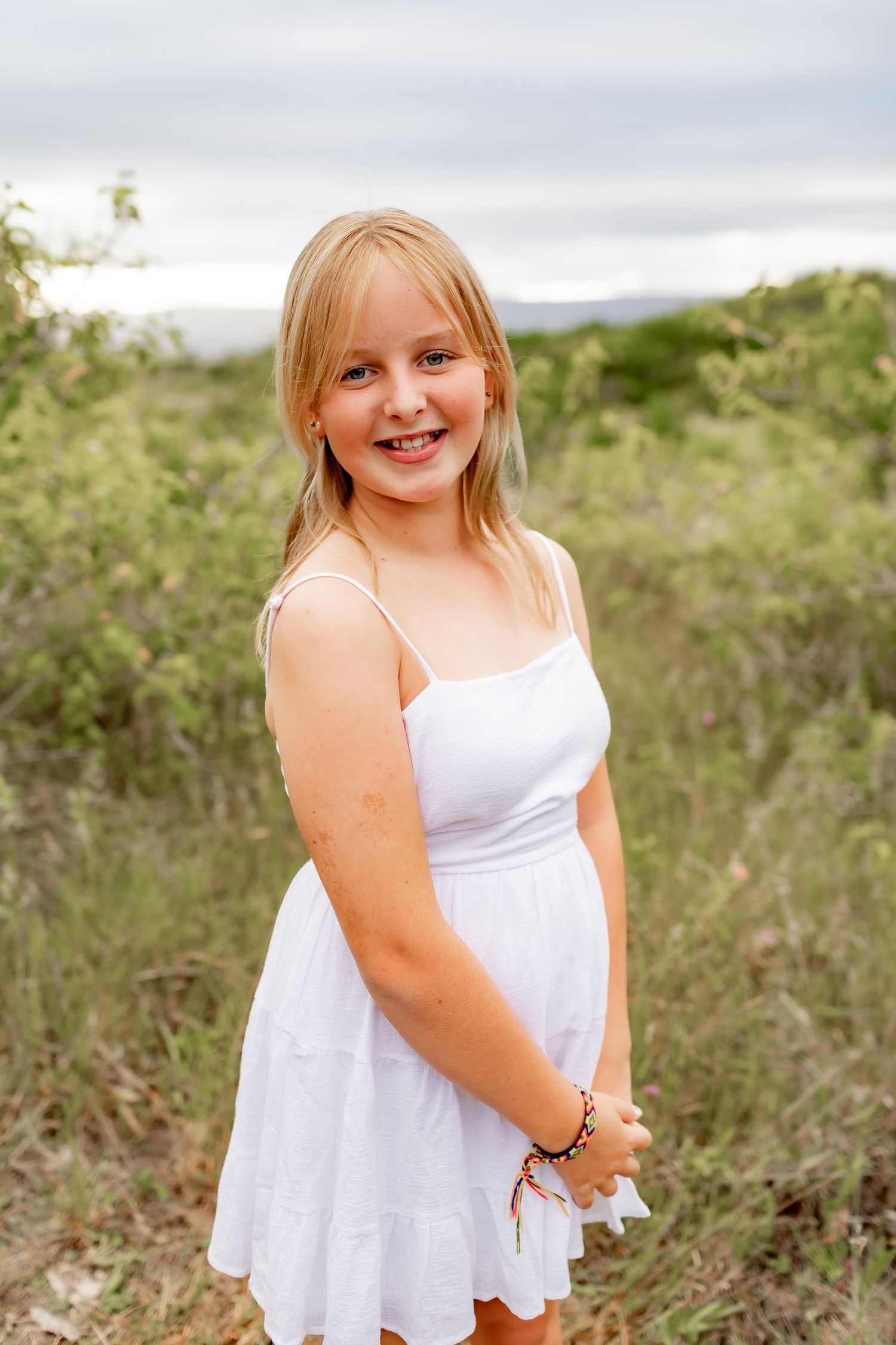 Young person in white summer dress poses against desert landscape backdrop.
