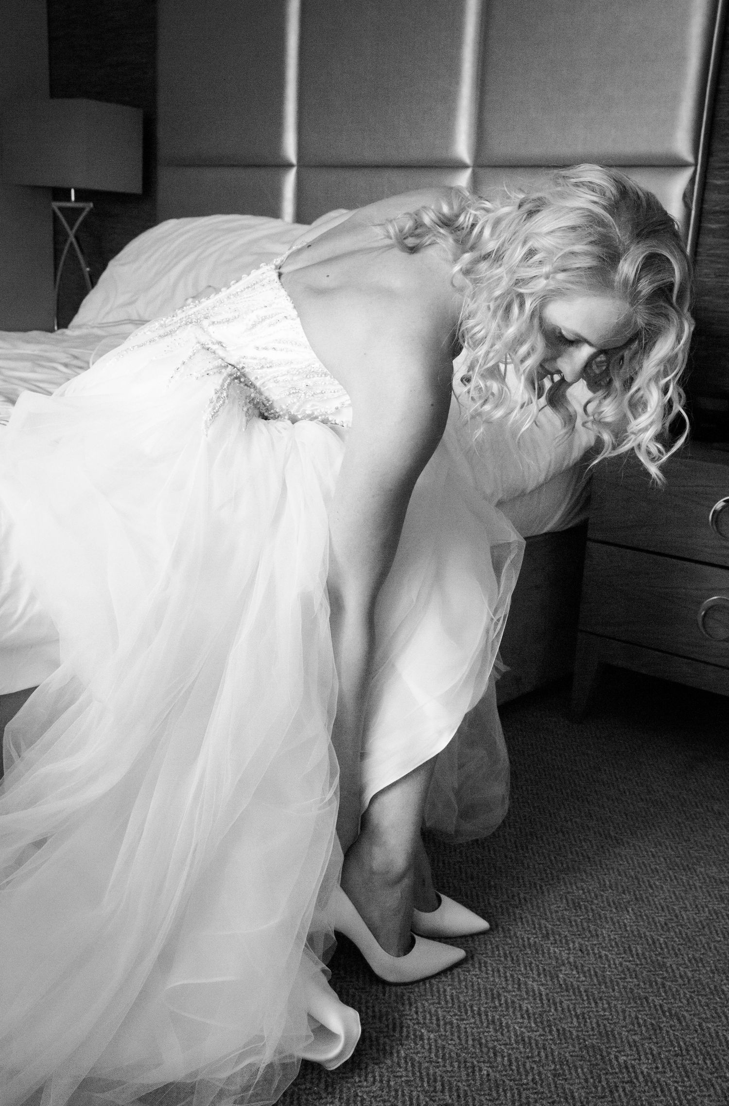 Black and white photo of bride adjusting her shoe while wearing flowing wedding gown.