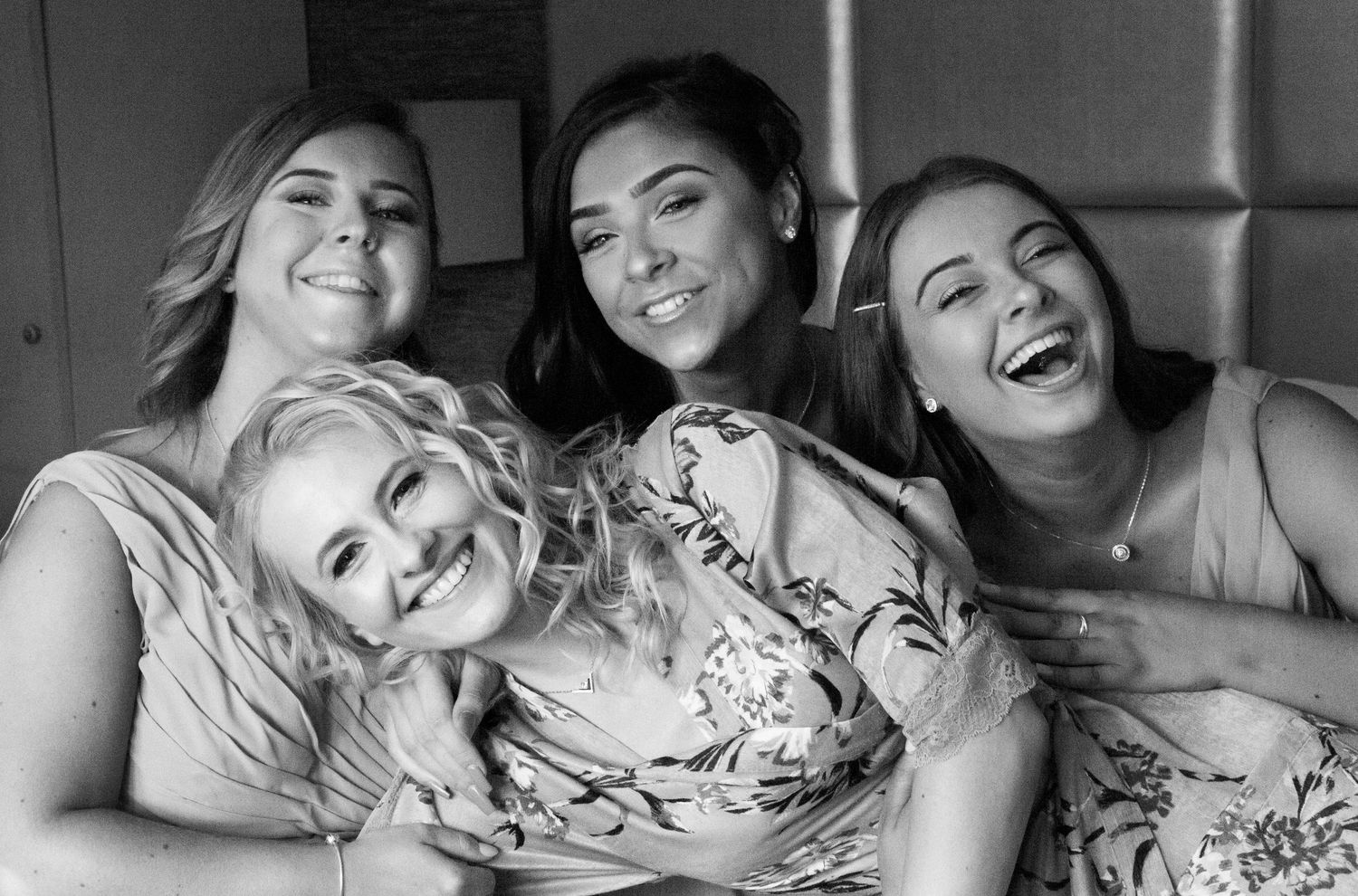 Group of bridesmaids and bride laughing together in black and white portrait.
