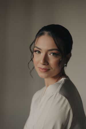 A soft, moody bridal portrait with elegant makeup and pulled-back dark hair against a neutral background.