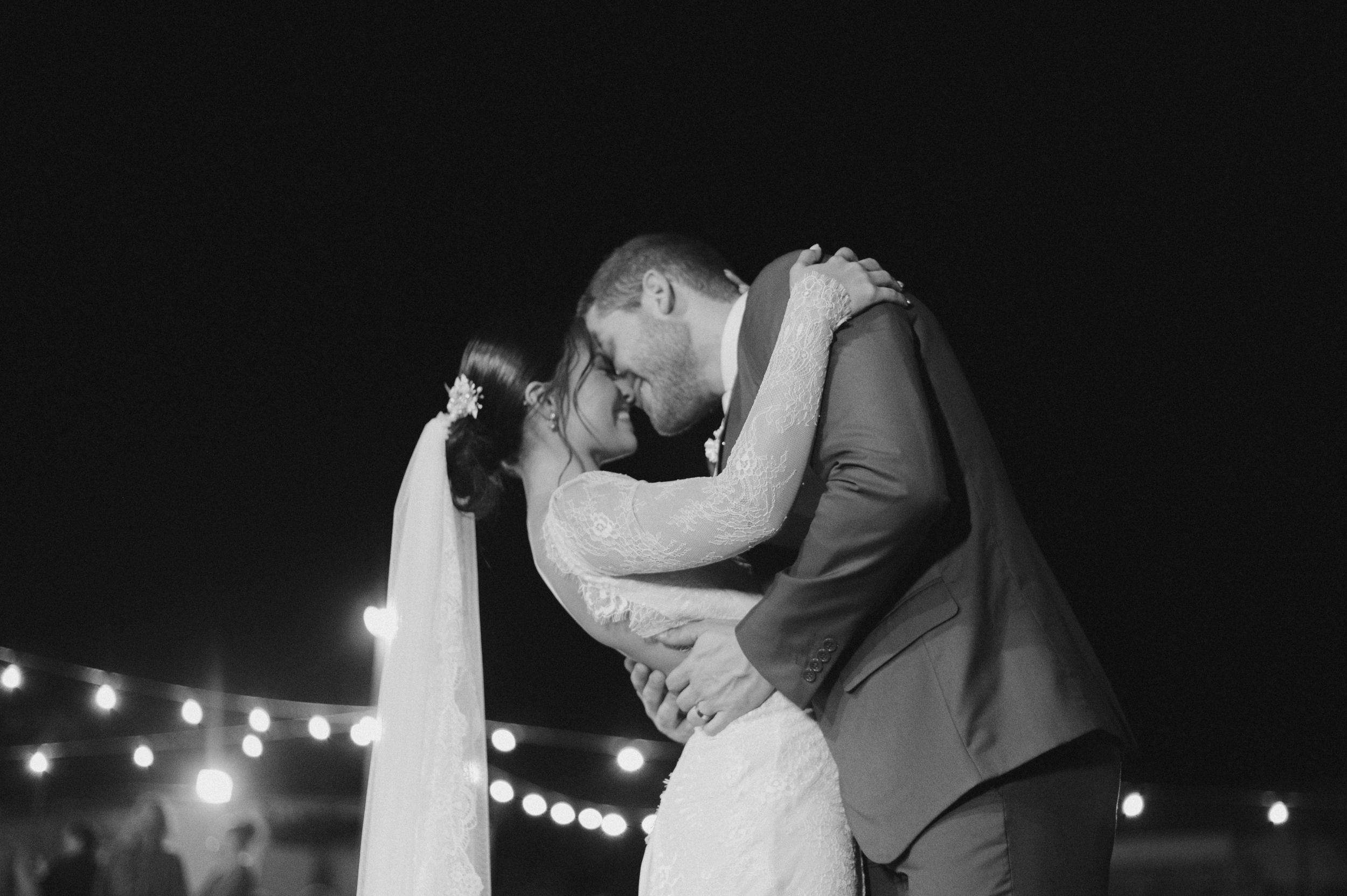 A romantic black and white wedding photo of a couple's intimate dance under twinkling lights.