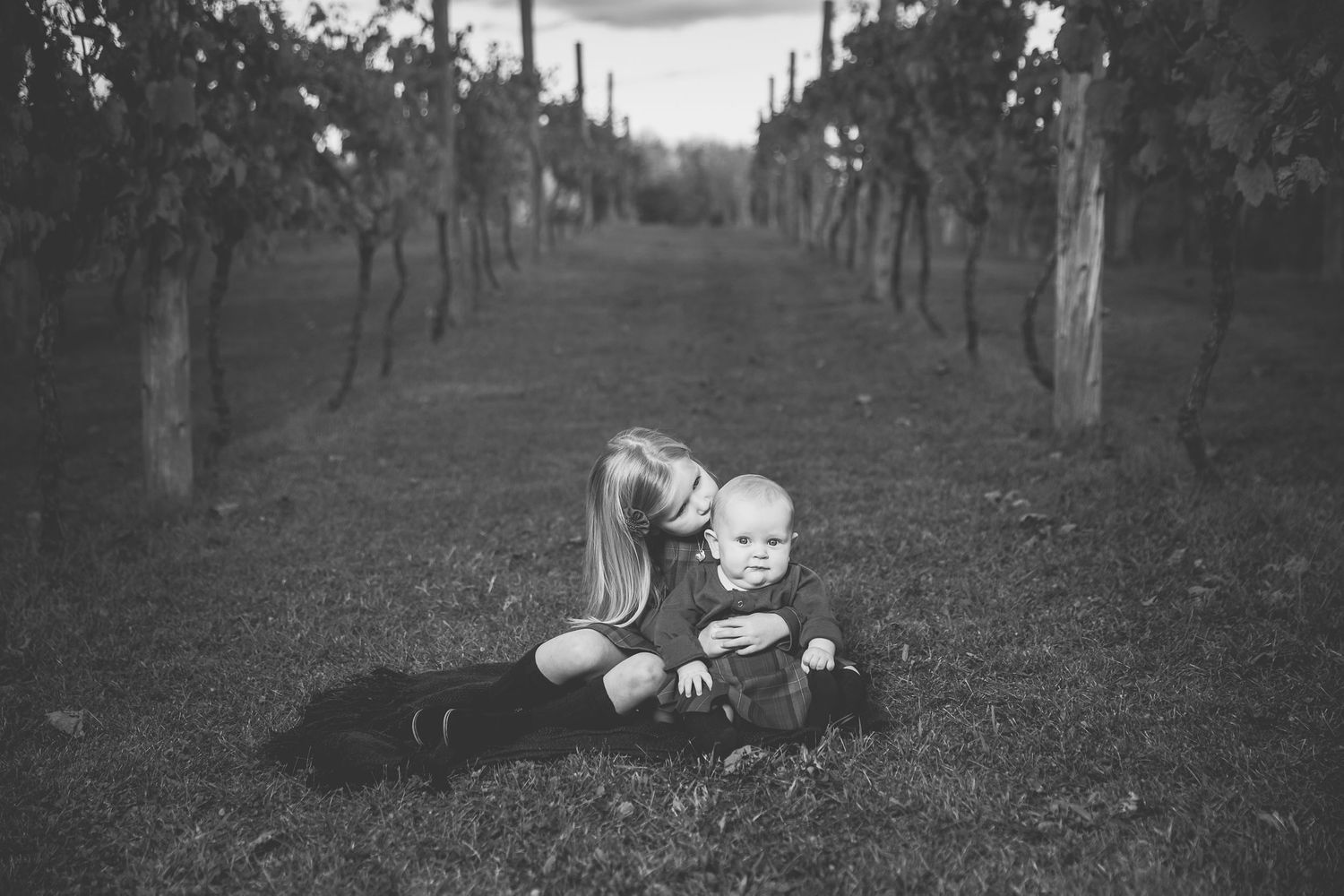 Black and white image showing affection in a vineyard under rows of grapevines.