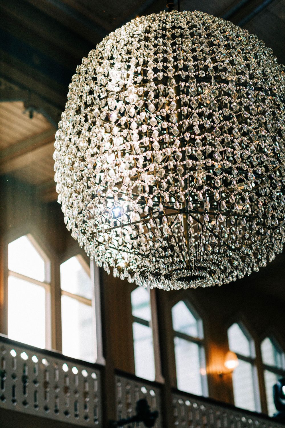 Large crystal chandelier hanging in an ornate room with arched windows and dramatic lighting.
