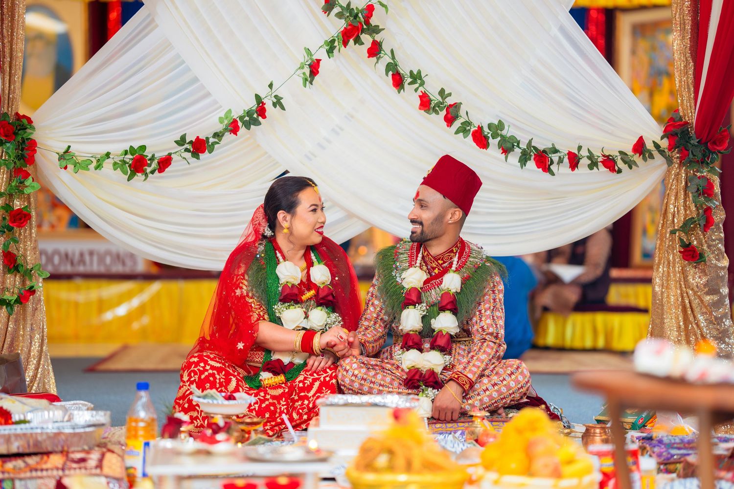 Traditional Hindu wedding ceremony with couple in red and cream attire under decorated mandap.