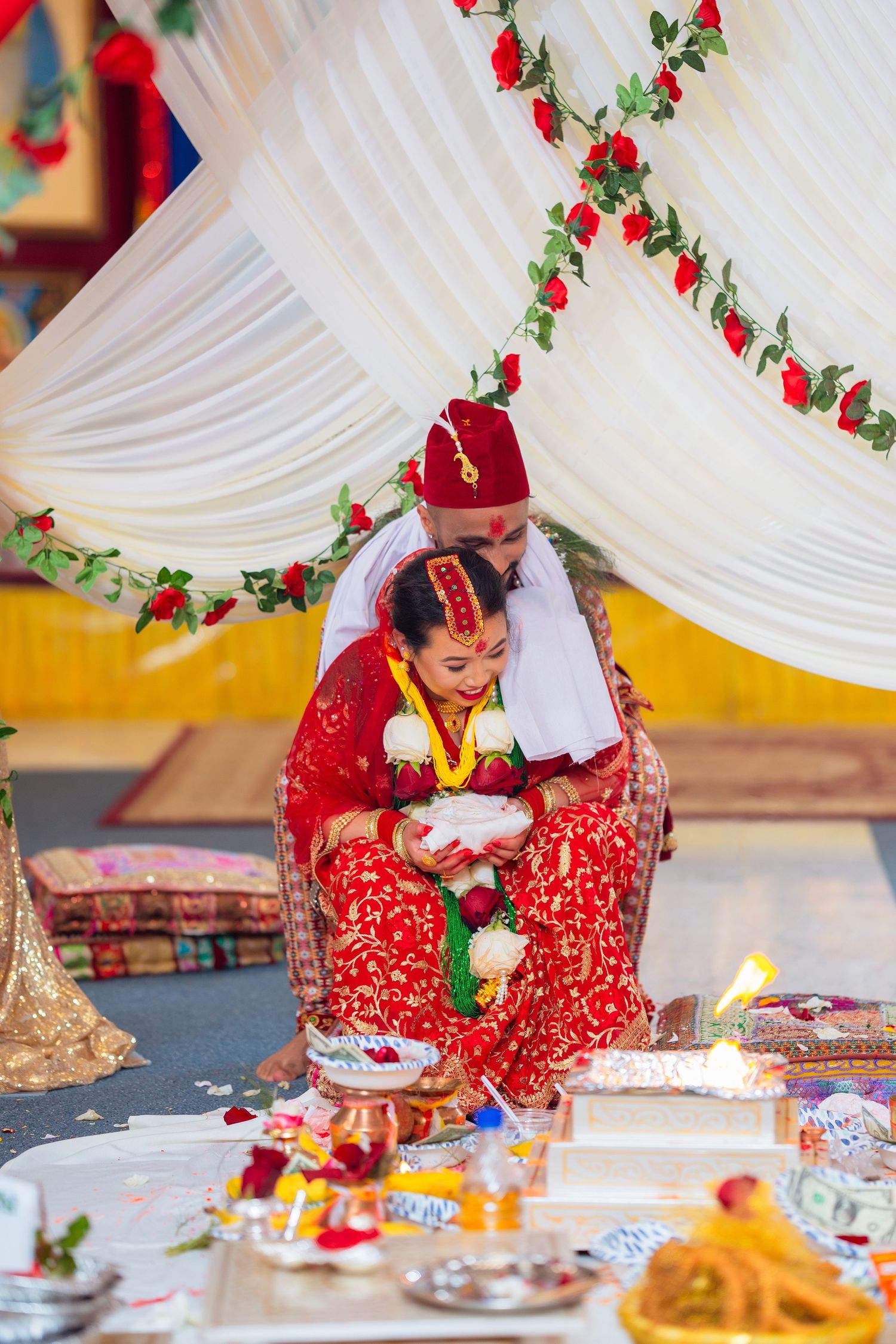 Traditional Hindu wedding ceremony with couple performing rituals under white and red decorated mandap.