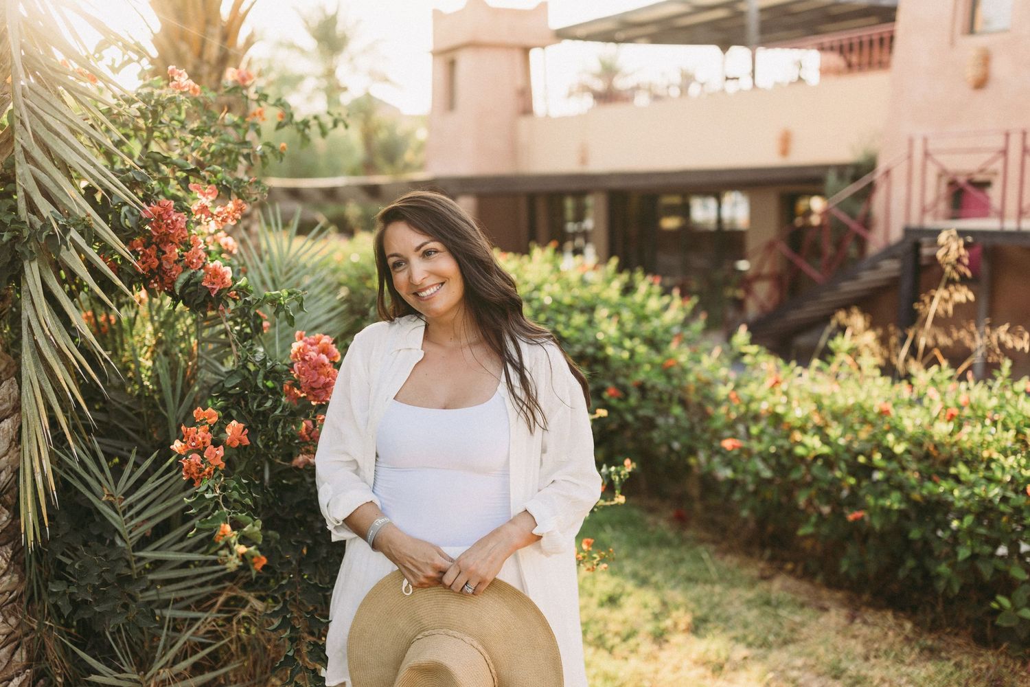 Person in white top and hat enjoying a sunny garden setting with tropical flowers.