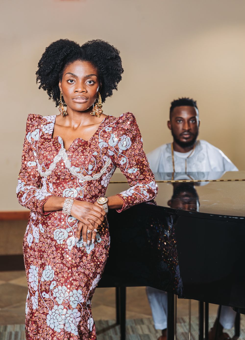 A person in a floral print dress poses near a grand piano during a photoshoot.