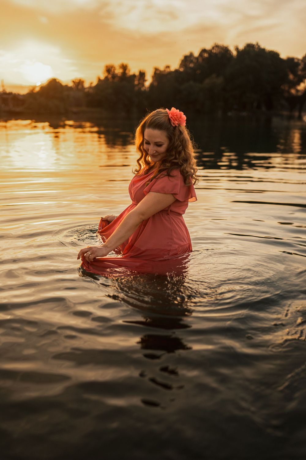A person in a flowing red dress twirls in lake water during golden hour.